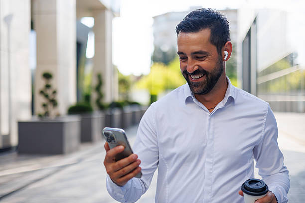 istock Happy businessman walking outdoors, using smartphone and wireless earbuds while holding a coffee cup 2228155369