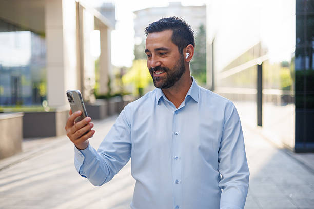 istock Businessman is smiling while making a video call on his smartphone, using wireless earphones, in a modern city setting 2228155908