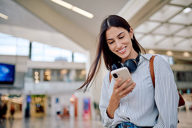 istock Young woman smiling while using mobile phone in airport terminal 2228157057