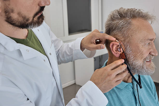 istock Audiologist meticulously fitting a hearing aid for elderly patient, using advanced equipment in a modern clinic setting. REM 2228159422