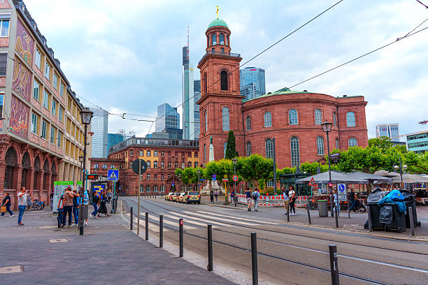 Frankfurt, Germany - June 10, 2025: Roemer, a historic building in Frankfurt, contrasts with contemporary skyscrapers amidst a busy urban street scene featuring pedestrians and vehicles.
