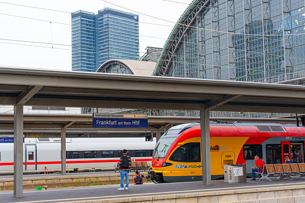 Frankfurt, Germany - June 10, 2025: Train station scene in Frankfurt, featuring a vibrant train, commuters, and modern skyscrapers under a cloudy sky.
