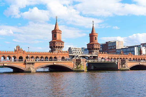 Berlin, Germany - May 30, 2025: Oberbaum Bridge features its iconic red brick towers, spanning the Spree River in Berlin, with a clear blue sky and modern buildings in the background.