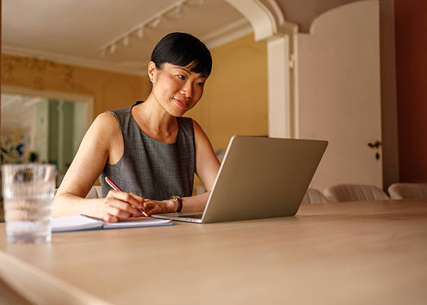 istock Confident female manager writing notes in book while researching on laptop at desk in corporate office 2228169415