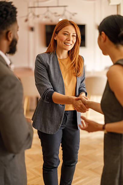 Smiling female executive welcomes colleagues with handshake in corporate office during team meeting
