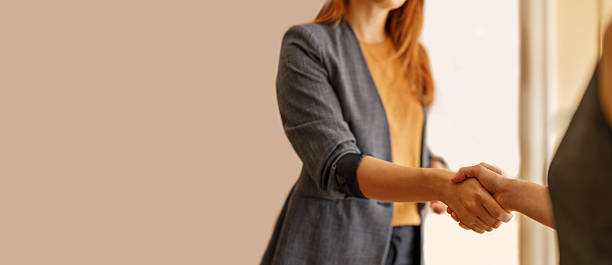istock Midsection of female professionals congratulating each other with handshake after successful meeting against wall in office 2228169544