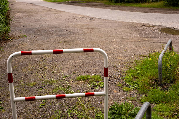 Red and white metal barrier blocking a damaged asphalt road, indicating restricted access