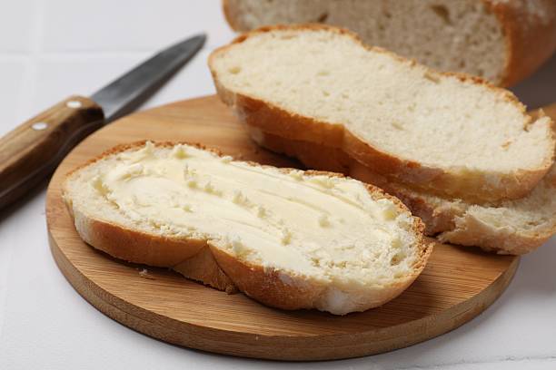 istock Fresh bread with butter and knife on white tiled table, closeup 2228177145