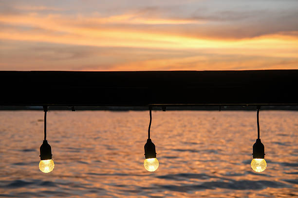 istock Close up of light bulb, hanging string light with bokeh sunset view along the river 2228181181