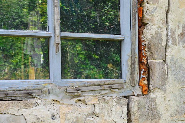 Old stone wall with rustic wooden window reflecting greenery, evoking rural charm and decay. Themes: countryside, nostalgia, rustic architecture, decay, reflection