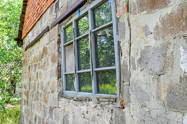 Old stone wall with rustic wooden window reflecting greenery, evoking rural charm and decay. Themes: countryside, nostalgia, rustic architecture, decay, reflection