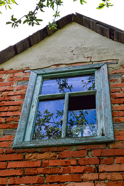 Old stone wall with rustic wooden window reflecting greenery, evoking rural charm and decay. Themes: countryside, nostalgia, rustic architecture, decay, reflection