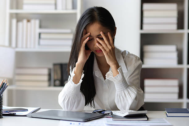 istock A woman in the office is stressed and has a headache from overwork. Tired business woman sleepy and bored from sitting at a desk for a long time and has office syndrome. 2228199708