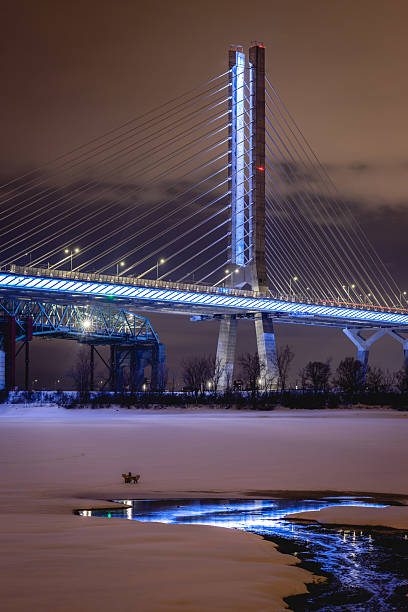 A nighttime winter view of Montreal's Champlain Bridge, beautifully illuminated above a frozen St. Lawrence River.