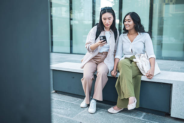 istock Two young women are using a smartphone and sitting on a bench 2228229333