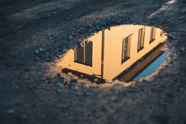 The reflection of a building in a puddle on a dirt road.