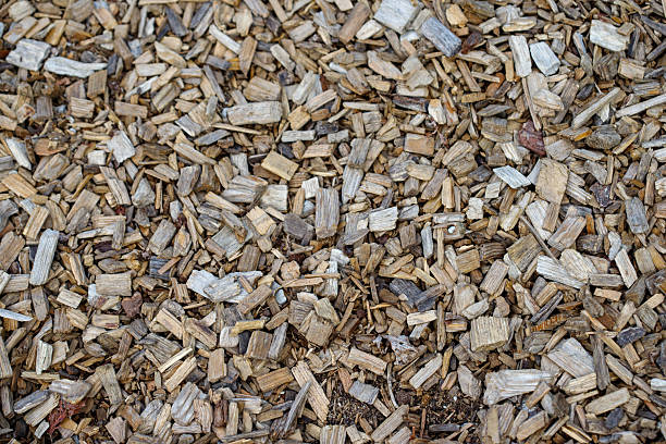 High-angle close-up of irregularly shaped wood chips filling the frame. Varied browns and grays are prominent.