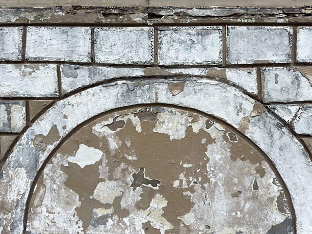Peeling paint and rough plaster on an old brick wall form textured background with weathered surfaces and visible damage. Perfect for design or architectural texture reference