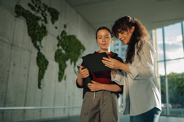 Teacher and student using digital tablet near green world map