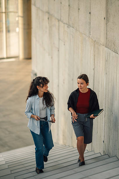 istock Two young businesswomen walking down stairs and talking about work 2228240513