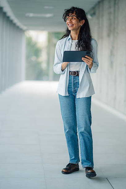istock Smiling businesswoman walking in modern office corridor using digital tablet 2228240624