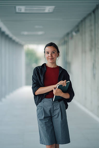 istock Young student holding a book and smiling in university hallway 2228240627