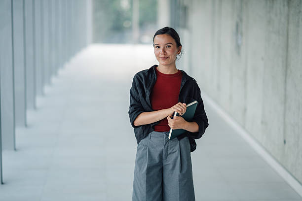 istock Young woman holding a notebook in a modern building corridor 2228240630