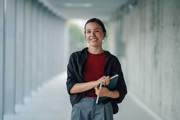 istock Smiling university student holding book in corridor 2228240632