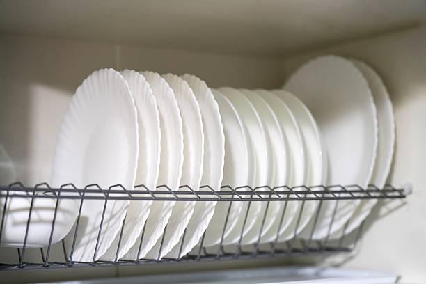 White ceramic plates stacked in a kitchen cabinet dish rack. Organized dish storage for drying and space-saving.