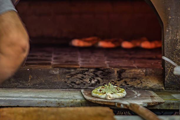 Fresh Turkish pide with savory topping rests on a wooden peel, ready for baking in a rustic stone oven, traditional food preparation, Istanbul, Turkey