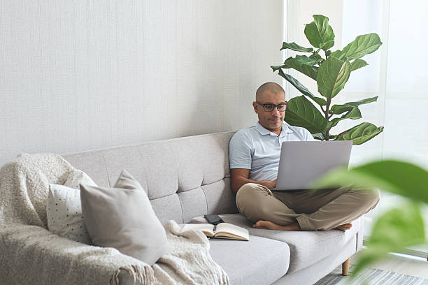 istock Focused man working from home, typing on laptop and sitting comfortably on sofa 2228243650