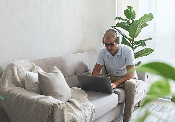 istock Man working from home sitting on the sofa using laptop and headphones 2228243656