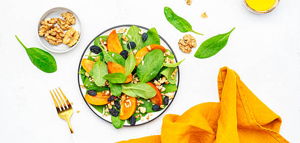 istock Yummy persimmon salad with walnuts, raisin and fresh spinach, white background, top view 2228245333