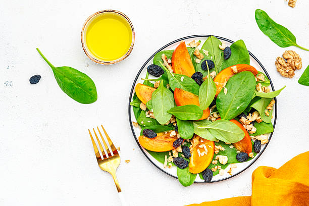 istock Yummy persimmon salad with walnuts, raisin and fresh spinach, white background, top view 2228245334
