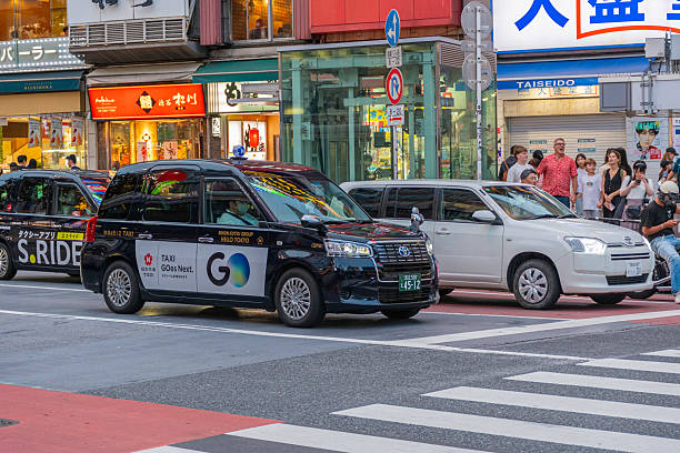 Japan. Nagoya. April 2, 2024. Black Japanese taxi, the car driver wearing a protective face mask and seated in the right side of the car