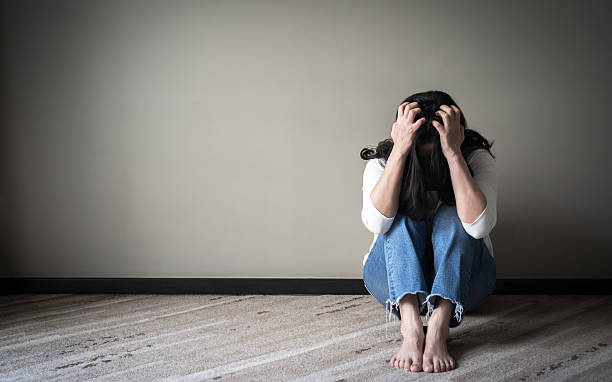 Panic attack woman, stressful depressed emotional person with anxiety disorder mental health illness, headache and migraine sitting against wall in domestic home floor #metoo (me too) concept stock photo