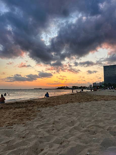 Golden sunset casting warm light over Waikiki Beach in Oahu, Hawaii, with the ocean reflecting vibrant orange and pink hues.