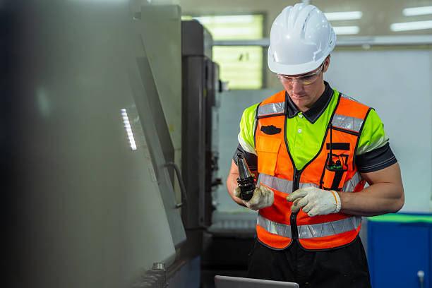 istock A man in a safety vest is working on a machine. Professional engineer engaged in precision manufacturing, preparing tooling and programming an industrial machine in a factory workshop. 2228260703