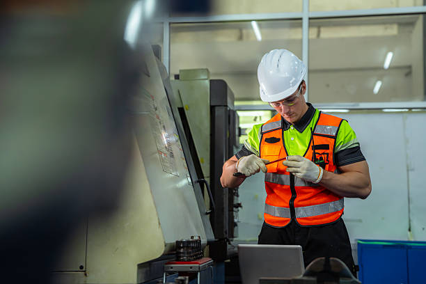 istock A man in a yellow and orange vest is working on a machine. Professional engineer engaged in precision manufacturing, preparing tooling and programming an industrial machine in a factory workshop. 2228260705