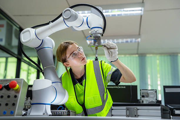 istock A woman in a yellow vest is working on a robot. Robotics engineer specializing in maintenance, carefully inspecting and adjusting the tooling of a modern robotic arm. 2228260792
