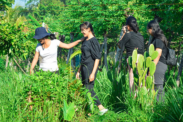 An Asian teenage boy examines moss-covered tree bark with a magnifying glass while his mother looks on during an eco-friendly forest hike. This scene reflects environmental education, green parenting, and sustainable travel.