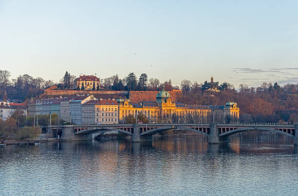 Prague, Czech Republic - December 5, 2024: Scenic view of the Vltava River with a historic bridge and riverside architecture during sunset, Prague, Czech Republic