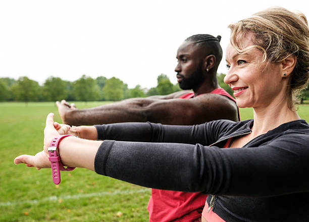 Two personal trainers stretching their arms in a park, enjoying the outdoors while preparing for a fitness session with clients. Emphasizing health and wellbeing, they embody motivation and energy