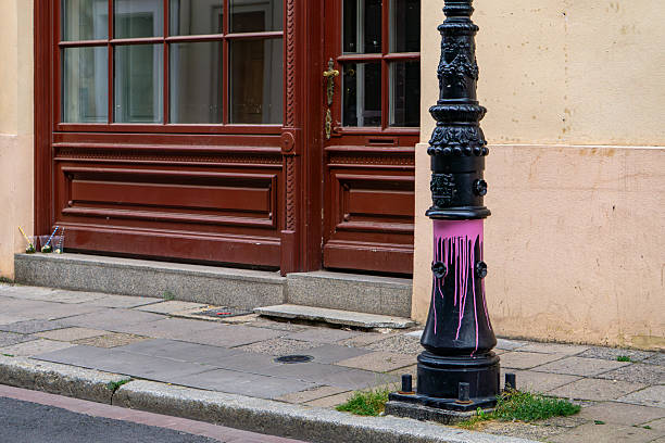 istock Vandalized street lamp sprayed with pink paint, located next to a historic building facade with wooden doors and a stone sidewalk. 2228273479