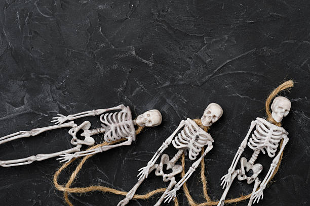 Plastic miniature skeletons hanging on jute rope against a textured dark background. Spooky Halloween-themed composition, perfect for seasonal design