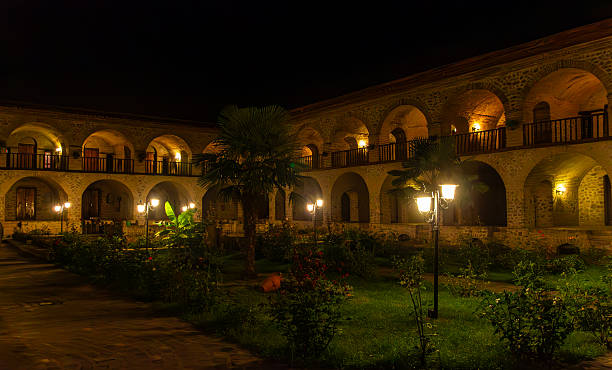 This image showcases a portion of the richly decorated facade of the Caravanserai in Sheki, Azerbaijan, highlighting its intricate architectural details. The facade features a mix of colorful mosaic tiles in geometric and floral patterns, along with finely crafted wooden windows and doors. The prominent archway entrance and overall design reflect traditional Azerbaijani artistry and heritage.