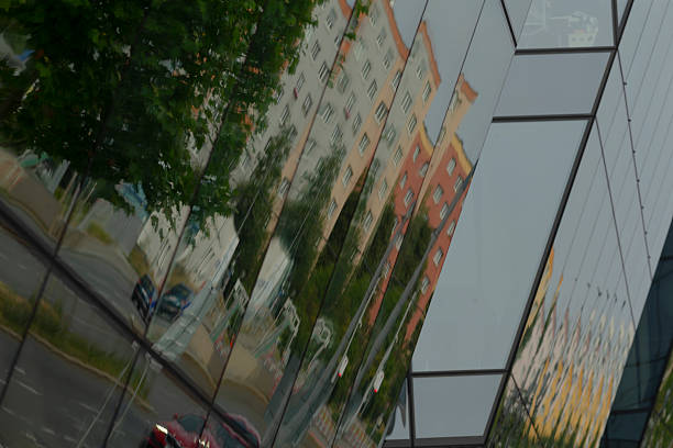A shiny red car is parked in front of a modern commercial building, which is beautifully reflected in the large glass facade