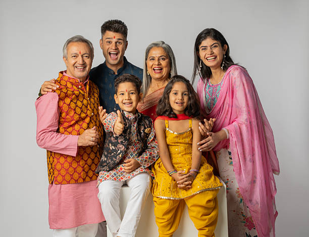 Cheerful rural indian family sitting on traditional bed at village home, excited little kids having fun with parents. daughter and son hug father and mother. happy life, playful children