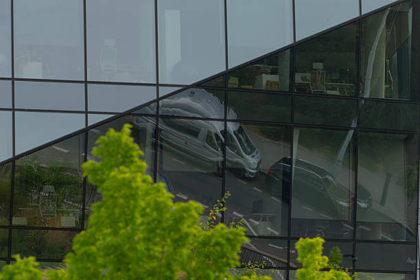 A van is beautifully reflected in the large glass windows of a modern building during the day, showcasing the contrast of materials and design
