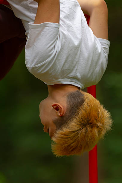 A young boy is performing an impressive handstand upside down while balancing carefully on a bright red pole that stands tall